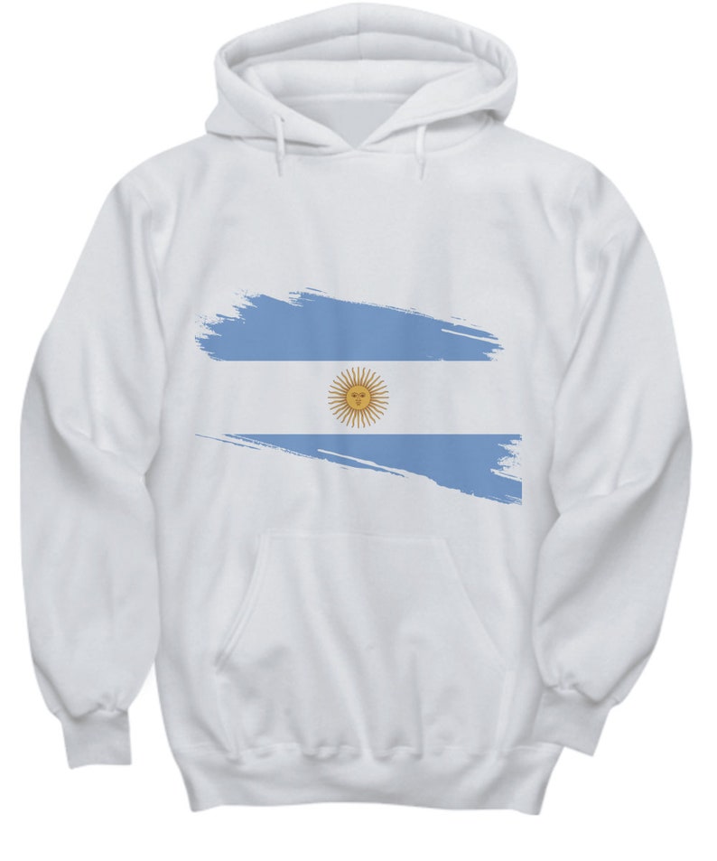 以下が含まれることがあります： 白地に青と白のアルゼンチン国旗のデザインが施されたフード付きスウェットシャツ。国旗は筆で描いたようなスタイルで描かれています。