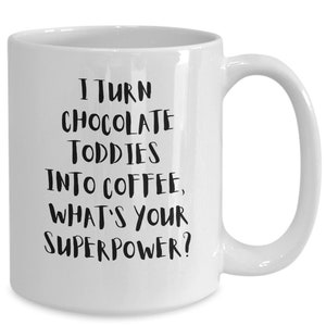 Könnte beinhalten: Weiße Keramik-Kaffeetasse mit schwarzem Text, der lautet: "Ich verwandele Schokoladen-Toddies in Kaffee, was ist deine Superkraft?"
