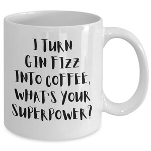 Könnte beinhalten: Weiße Keramik-Kaffeetasse mit schwarzem Text, der lautet: "Ich verwandele Gin Fizz in Kaffee, was ist deine Superkraft?"