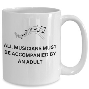 Pode incluir: Caneca de café de cerâmica branca com um design de nota musical preta e o texto "ALL MUSICIANS MUST BE ACCOMPANIED BY AN ADULT".
