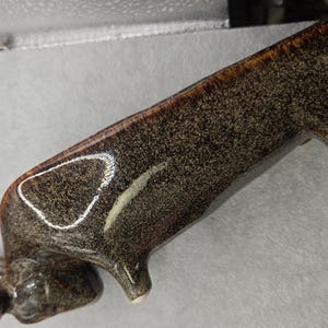 May include: A ceramic planter in the shape of a bull, with a speckled brown glaze and a glossy finish. The planter has a long trough for planting and is supported by three small legs. The bull's head is at one end, with horns and a detailed face.