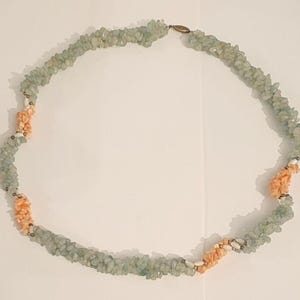 Puede incluir: Un collar de piedras verdes y melocotón con un cierre plateado. El collar está hecho de pequeñas piedras de forma irregular.