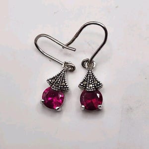 May include: A pair of silver earrings with a pink gemstone and a marcasite design.