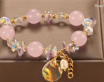 May include: A pink and gold bracelet with a crystal seashell charm. The bracelet is made with pink beads, clear crystals, and gold spacers.