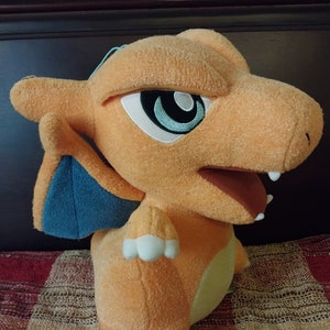 May include: Orange and blue plush toy of a dragon-like Pokemon character with a wide open mouth and white claws.