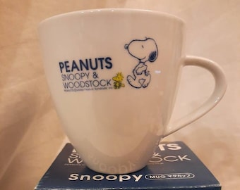 Può includere: Tazza in ceramica bianca con un design Peanuts Snoopy e Woodstock blu e bianco. La tazza è in una scatola blu con lo stesso design e il testo "PEANUTS SNOOPY & WOODSTOCK" e "MUG マグカップ".