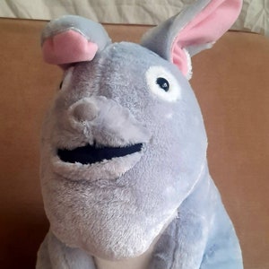 Op de afbeelding: Een pluche grijs en wit konijn met grote oren en een brede glimlach. Het konijn heeft zwarte ogen en een zwarte mond.