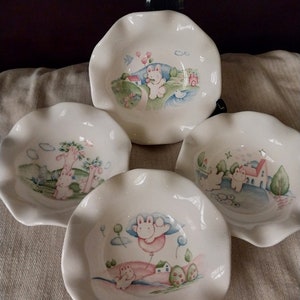 Puede incluir: Conjunto de cuatro cuencos de cerámica blanca con bordes festoneados. Cada cuenco presenta un diseño diferente pintado a mano de un conejito en un entorno caprichoso con colores pastel.