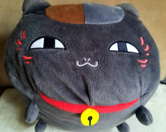May include: A plush grey cat toy with brown and grey fur, red embroidered details, and a red collar with a yellow bell.