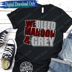 May include: Black t-shirt with the text "WE BLEED MAROON & GREY" in maroon and grey. The shirt is displayed with black sneakers and blue jeans on a white wooden surface. The words "Digital Download Only" are at the top.