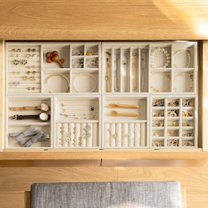 May include: A beige velvet jewelry organizer tray set with multiple compartments, slots, and ring rolls. The tray contains various items including gold and silver necklaces, bracelets, wristwatches, stud earrings, hair bows, and small wooden utensils.