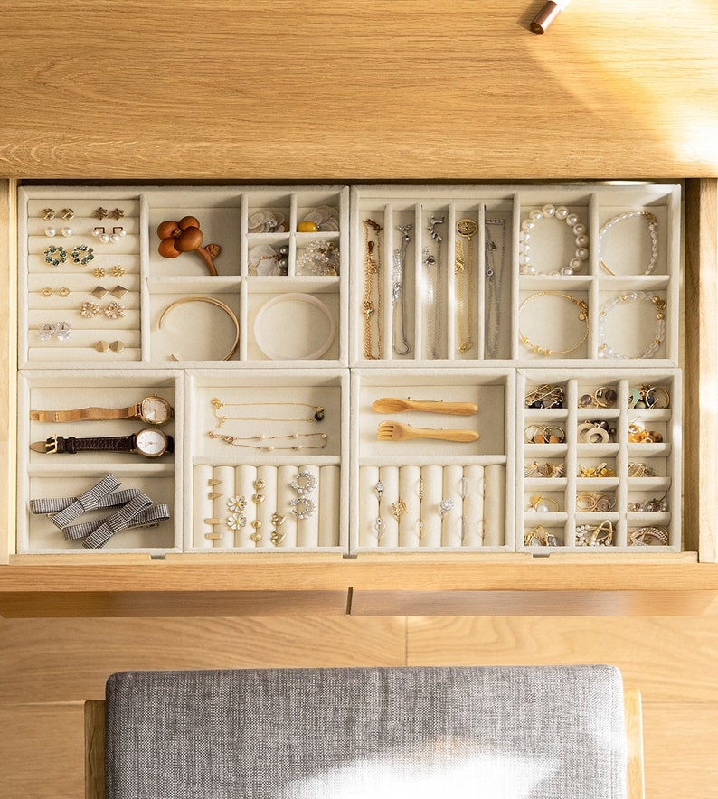 May include: A beige velvet jewelry organizer tray set with multiple compartments, slots, and ring rolls. The tray contains various items including gold and silver necklaces, bracelets, wristwatches, stud earrings, hair bows, and small wooden utensils.
