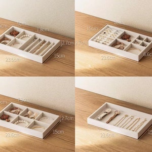 May include: A rectangular beige jewelry organizer tray with multiple compartments for storing accessories. The tray measures 23.6 cm in length, 15 cm in width, and 2.7 cm in height. It features various internal dividers to hold watches, bracelets, rings, and necklaces.