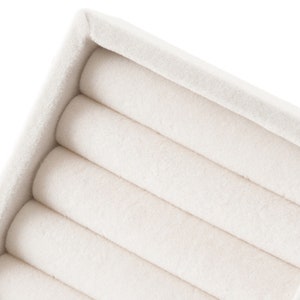May include: A cream-colored jewelry display tray featuring five parallel, soft-textured, cylindrical velvet rolls designed for organizing rings or small accessories, set within a matching rectangular frame with a clean, neutral finish.