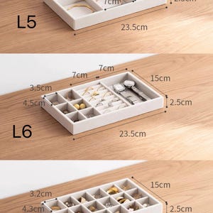 May include: Three beige velvet jewelry organizer trays labeled L5, L6, and L7. Each tray measures 23.5cm by 15cm by 2.5cm. L5 has six compartments, L6 has twelve, and L7 has twenty-four. The trays contain various rings, watches, and earrings.