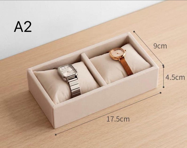May include: A beige velvet watch display tray labeled A2 with two compartments, each containing a soft cushion. One cushion holds a silver-tone watch with a metal link band, and the other holds a gold-tone watch. Dimensions are 17.5cm by 9cm by 4.5cm.