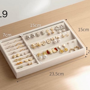 May include: A beige velvet jewelry organizer tray labeled L9, measuring 23.5 cm by 15 cm by 2.5 cm. The tray features a left section for rings and a right section for earrings, with a 7 cm and 5 cm internal divider width visible.