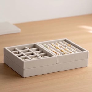 May include: A light gray velvet jewelry organizer tray featuring two distinct sections. The left side contains a grid of square compartments, while the right side features multiple padded slots designed to hold rings and small earrings securely.