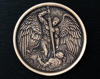 May include: Bronze-colored round coin featuring a detailed relief of an angel with large wings, holding a sword over a figure. The coin has a raised edge and is set against a dark background.