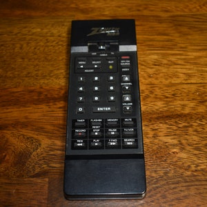 May include: A black Zenith remote control with a variety of buttons, including number keys, channel up and down, volume up and down, play, pause, rewind, fast forward, and more.