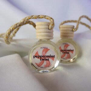 May include: Two small glass bottles with a peppermint twist design and a white string for hanging. The bottles are filled with a clear liquid and have a wooden cap. The bottles are labeled "Peppermint Twist" and "Car Diffuser 18ml".