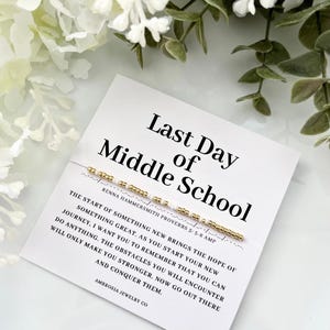 Peut inclure: Carte blanche avec du texte noir qui dit "Dernier jour du collège". Un bracelet en perles dorées avec des perles blanches est sur la carte. La carte comprend également une citation de Proverbes 3:5-6 AMP.