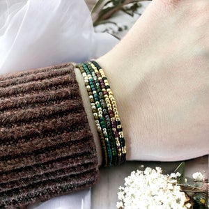 May include: A stack of colorful beaded bracelets in shades of green, gold, and brown. The bracelets are layered on a person's wrist.