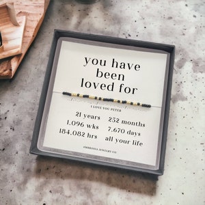 May include: A black gift box with a card and a beaded bracelet. The card says "you have been loved for" with a Morse code message. Additional text includes "I love you Peter" and time measurements.