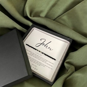 May include: A black box with a white card inside. The card has the name "John" written in cursive and a message that reads "I love you. Your parents, we have been blessed to witness your every triumph, and even your struggles. We couldn't be more proud of who you have become. Take on a new role and marry the love of your life, know that we are always behind you every step of the way. With love, Mom & Dad."