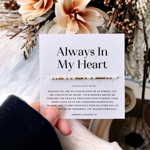 May include: White card with the text "Always In My Heart" and a small beaded bracelet with gold and white beads. The card has a message about remembering someone who is no longer with you. The card also includes the text "Always In My Heart" and "Ambrosia Jewelry Co."