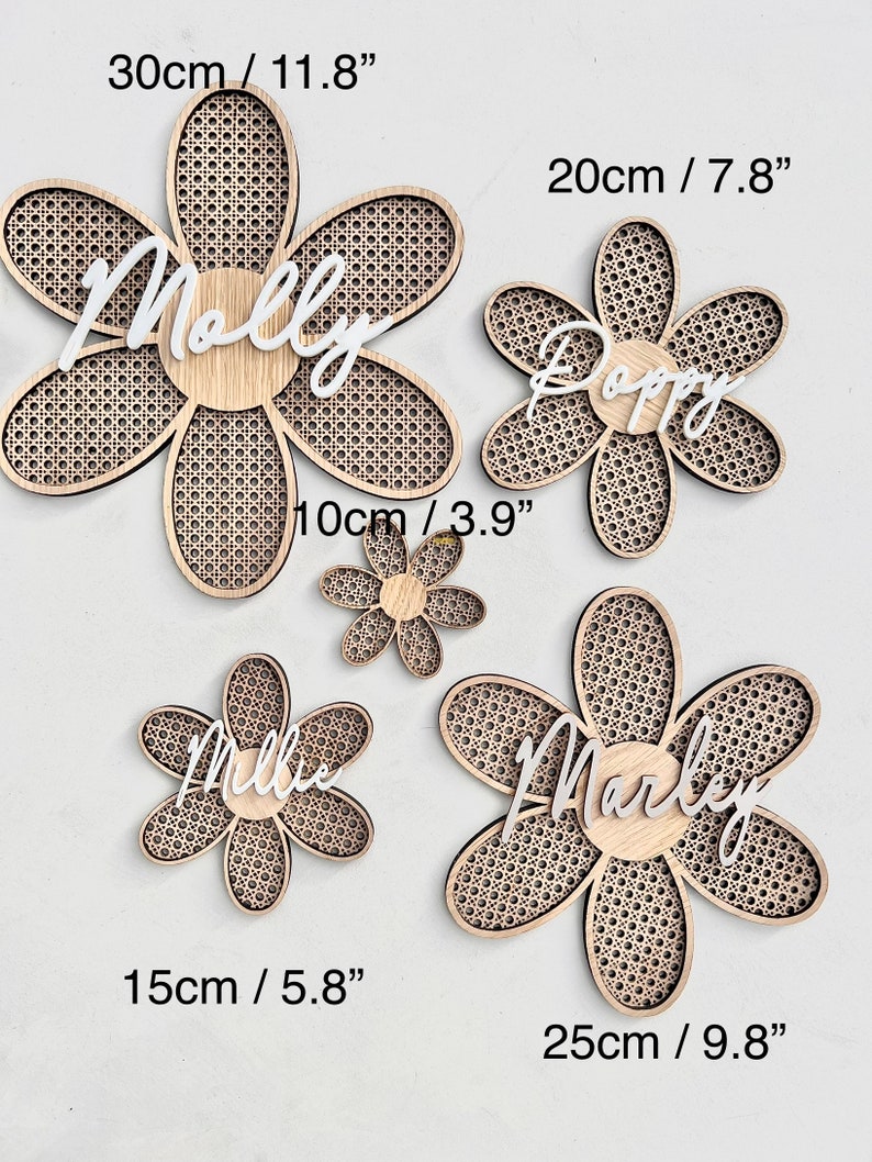 K&ouml;nnte beinhalten: Vier h&ouml;lzerne, blumenf&ouml;rmige Wanddekorationen mit verschiedenen Namen darauf. Die Namen sind Molly, Poppy, Millie und Marley. Die Blumen haben einen Durchmesser von 30 cm, 20 cm, 15 cm und 25 cm.