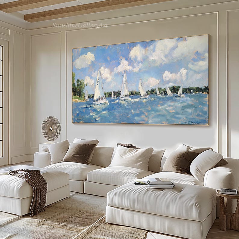 Op de afbeelding: Een schilderij van een zeegezicht met zeilboten op een blauwe watermassa. De lucht is blauw met witte wolken. Het schilderij is ingelijst en hangt aan een witte muur boven een witte bank.
