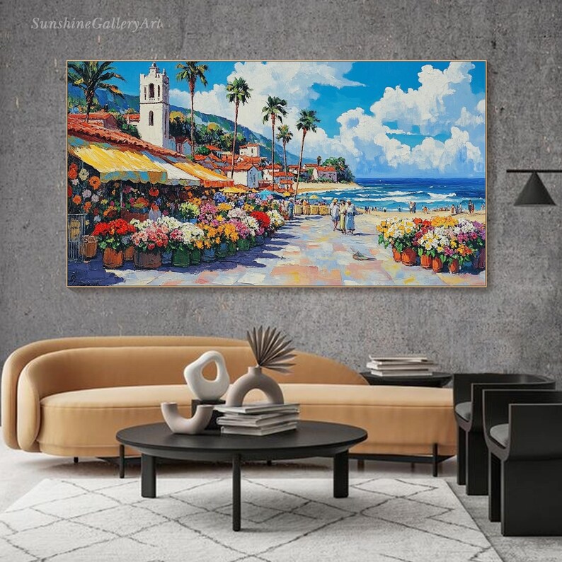 May include: A colorful painting of a seaside town with a white church, palm trees, and a beach with people walking along the shore. The painting is framed and hanging on a wall.