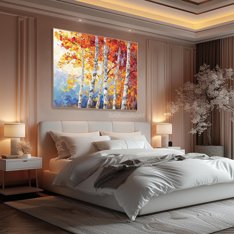 Puede incluir: Una cama blanca con una manta gris y almohadas blancas en un dormitorio con una pintura de un bosque de abedules con hojas naranjas, amarillas y rojas colgada en la pared. La pintura est&aacute; enmarcada en oro.