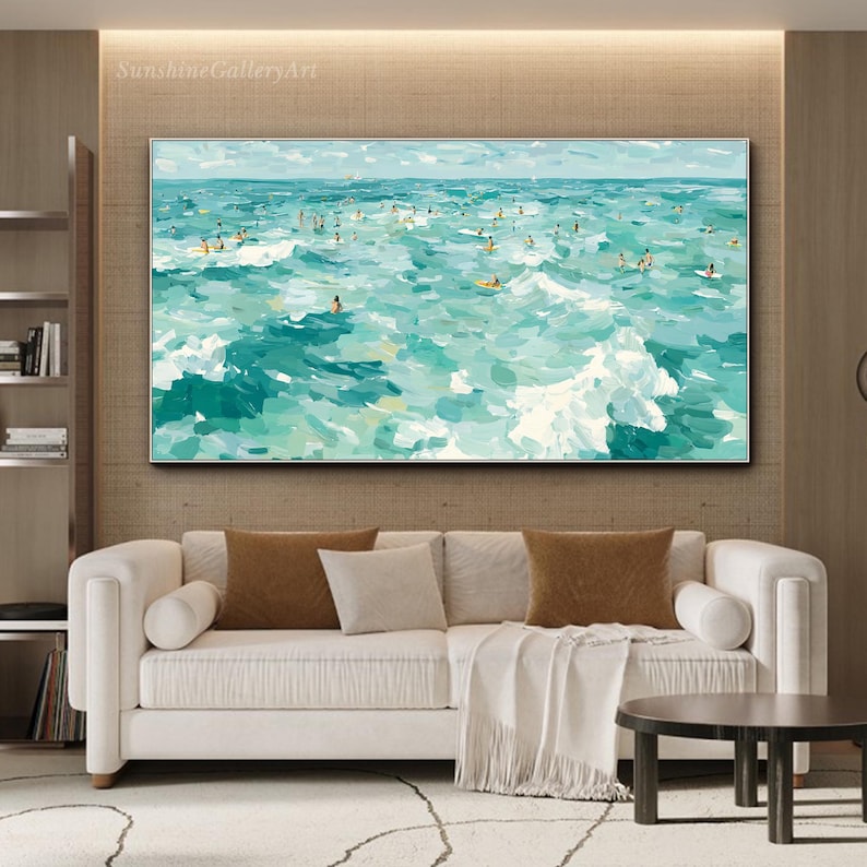 May include: An abstract painting of a turquoise ocean scene with numerous figures, possibly surfers or swimmers, scattered throughout the waves. The artwork, framed in a silver border, hangs above a white sofa with brown and beige pillows.