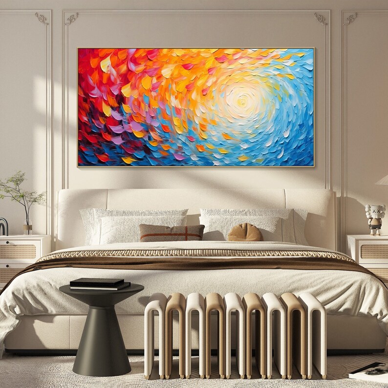 May include: Abstract painting with swirling colors of red, orange, yellow, blue, and purple. The painting is framed in gold and hangs above a white bed with a brown blanket and white pillows.