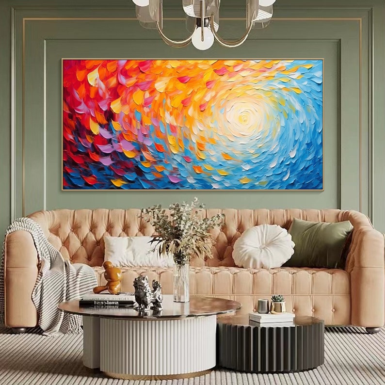 May include: Abstract painting with a swirling pattern of colorful brushstrokes in shades of red, orange, yellow, blue, and purple. The painting is framed and hanging on a wall above a beige sofa.