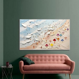 May include: A painting depicting a beach scene with white waves, blue sky, and colourful umbrellas. People are shown in the painting, enjoying the beach.