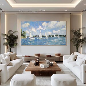 Op de afbeelding: Een schilderij van een zeezicht met witte zeilboten op een blauwe watermassa. De lucht is blauw met witte wolken. Het schilderij is ingelijst en hangt aan een muur in een woonkamer.