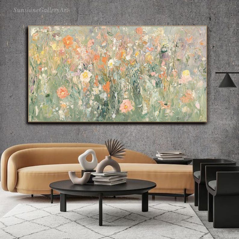 Op de afbeelding: Een abstract bloemenschilderij met een gouden lijst. Het kunstwerk toont een veld met bloemen in tinten oranje, roze, geel en wit tegen een groene en grijze achtergrond. Het schilderij wordt boven een gele bank getoond.