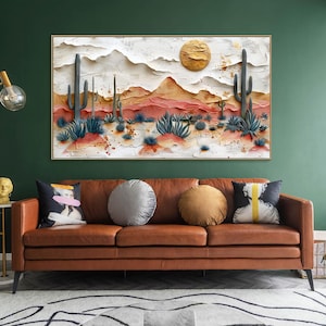 May include: A brown leather sofa with three cushions, two round and one rectangular. The sofa is in front of a green wall with a framed painting of a desert landscape with cacti and a golden sun.