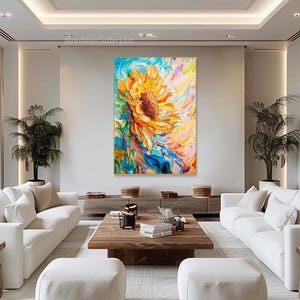 May include: A colorful abstract painting of a sunflower with yellow petals and a dark brown center. The background is a mix of blue, green, and pink hues. The painting is framed in a gold frame and is hanging on a white wall.
