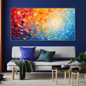 May include: Abstract painting with a swirling pattern of red, orange, yellow, blue, and purple. The painting is framed in gold and hangs on a blue wall.