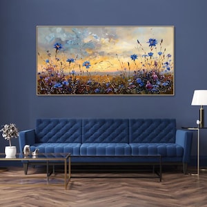 以下が含まれることがあります： 夕焼け空の下の青い花の野原を描いた油絵。 金色のフレームに入ったこのアートワークは、青いベルベットのソファの上に飾られています。 絵画の色使いは青、黄、茶色で、穏やかな風景を作り出しています。