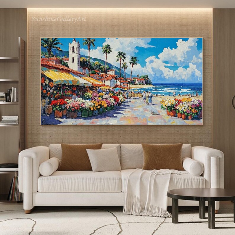 May include: A colorful painting of a seaside town with a white building and a blue sky. The painting features a flower market with colorful flowers and a beach with people walking on the sand.