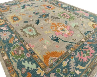 May include: A vintage rug with a light gray background and a teal border. The rug features a floral pattern with pink, orange, and green accents.