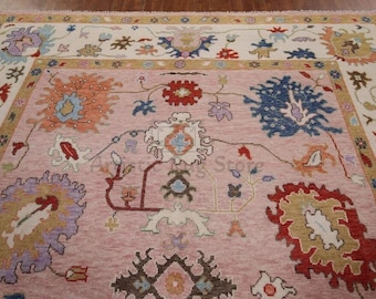 May include: A pink rug with a floral pattern in shades of blue, red, orange, and white. The rug has a cream-colored border with a floral design.