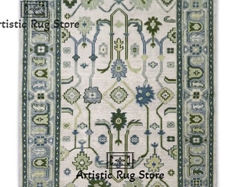 May include: A cream-colored rug with a blue and green geometric pattern. The rug has a fringe border and is decorated with floral motifs.