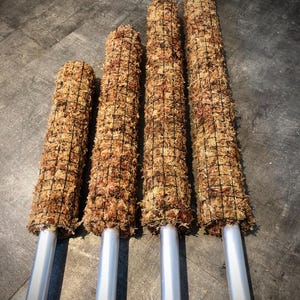 Op de afbeelding: Vier mosstokken in verschillende maten, elk omwikkeld met een draadgaas en gemonteerd op een zilveren metalen paal. De mosstokken zijn lichtbruin van kleur en zijn gerangschikt in een rij van de kleinste tot de grootste.