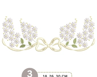 May include: An embroidery design featuring two clusters of white daisy flowers with yellow centers and green leaves, connected by a cream-colored ribbon tied in a central bow. The text 3 Sizes 18, 26, 30 CM is displayed in a rounded box.